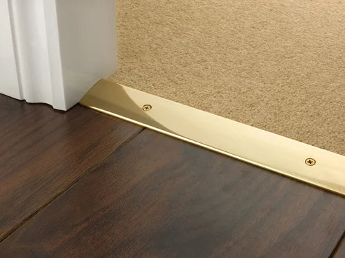 Curved-edge brass transition strip connecting dark wood to carpet flooring, secured with visible screws for durability.