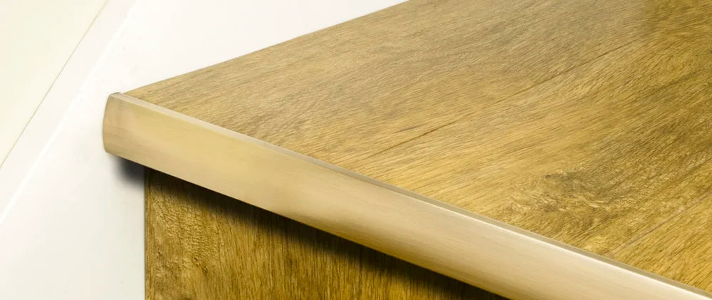 Premier Trims LVT Nosings in brushed brass finish installed on light oak stair edge for LVT stair protection and enhanced durability.