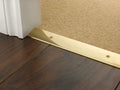 Curved-edge brass transition strip connecting dark wood to carpet flooring, secured with visible screws for durability.
