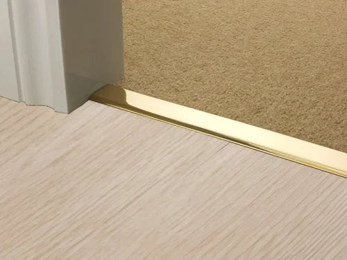 Polished brass transition strip between light wood and beige carpet flooring, designed for seamless room transitions.