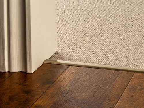 Brass flooring transition strip connecting dark wood and light carpet, ideal for doorways and room transitions.